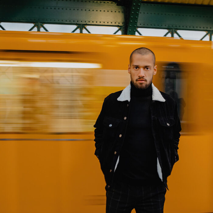 Ein Mann mit schwarzem Outfit steht von einer wegfahrenden U-Bahn die durch die Bewegung verschwommen ist