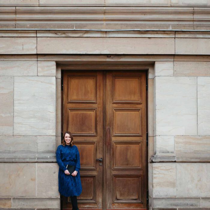 Frau steht für Business Portraits in einem Türrahmen und hält ein Notizbuch in der Hand